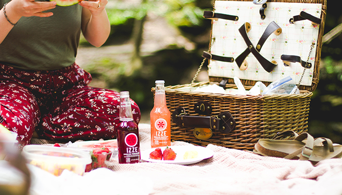 Image of lady sitting on picnic blanket with bottles and basket