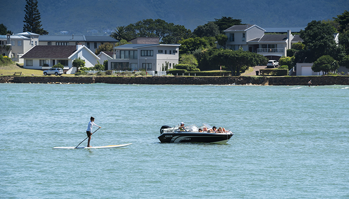 Person paddleboarding on the Knysna Lagoon with a boat and houses in the background