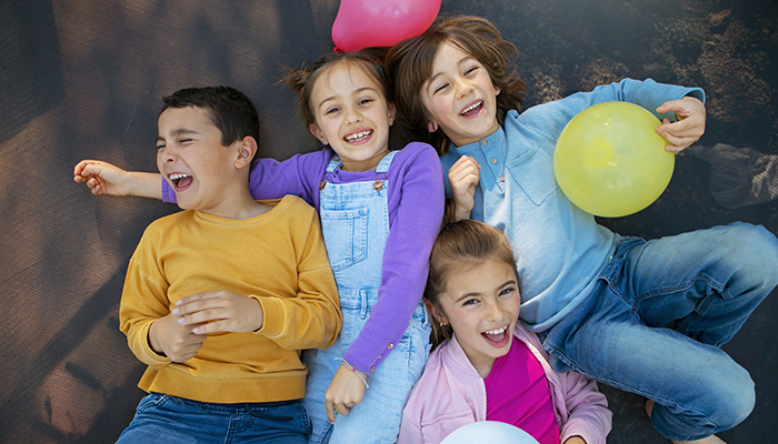 Four children laughing and playing with balloons at an outdoor festival
