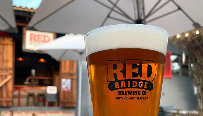 Glass of local IPA in front of Red Bridge Brewing Co. in Knysna