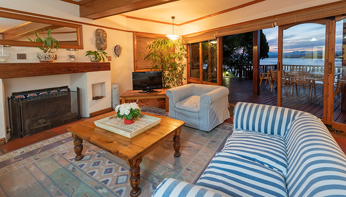 Paquita beach house lounge with fireplace, coastal décor, and sliding doors opening onto a deck overlooking the Knysna Lagoon.